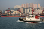 Containerschiff und Schlepper im Hafen von Hongkong vor Hochhusern