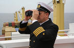Kapitän mit Fernglas auf der Brückennock des Containerschiffs